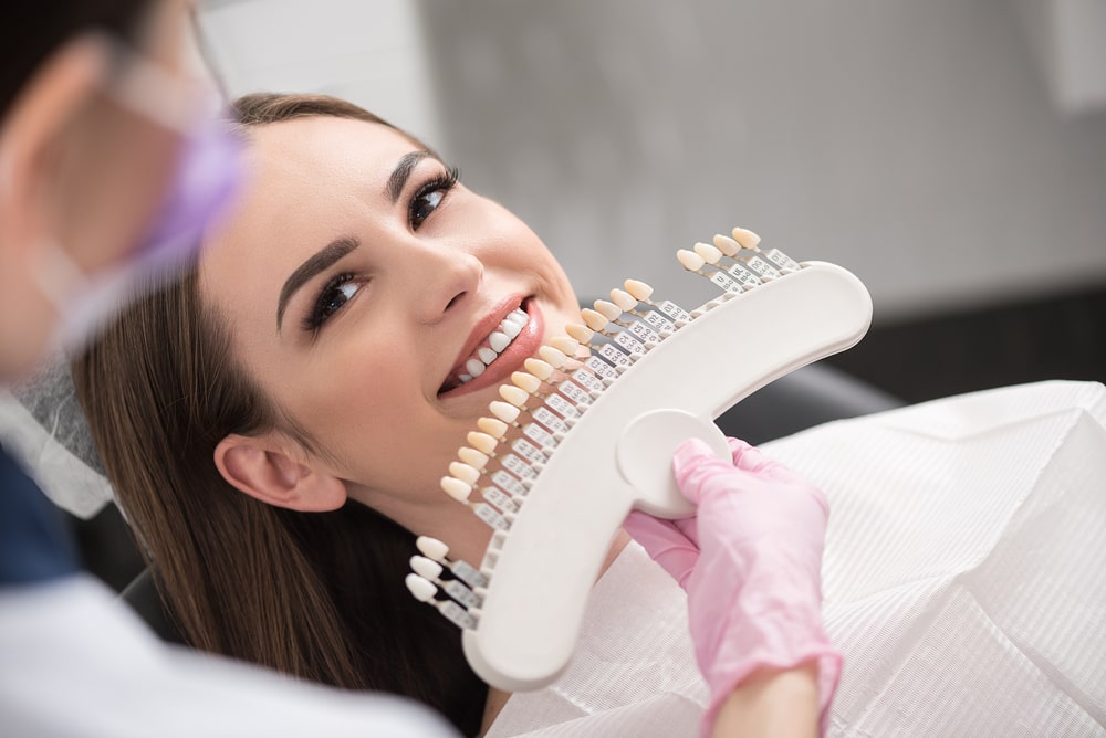 Dentist Comparing A Set Of Dental Crowns To Womans Teeth
