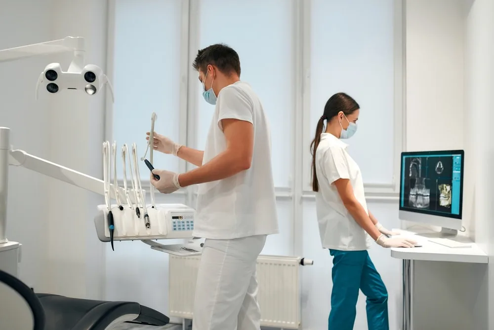 Young dentist prepares tools for work while assistant examines x-ray on a computer. Dentistry and dental care.