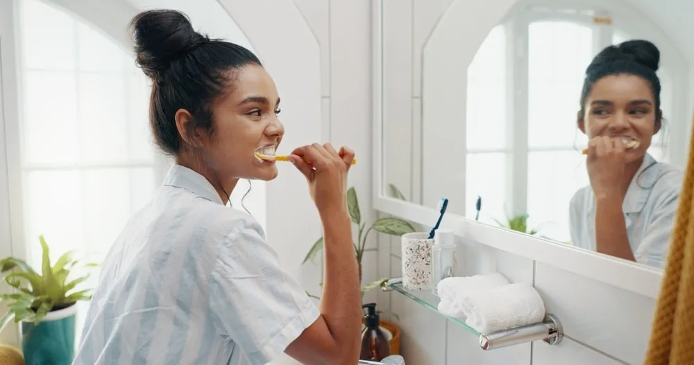 Mirror, home and woman brushing teeth, grooming and hygiene with morning routine. Person, reflection and girl with toothbrush, fresh breath and cleaning mouth with wellness and whitening in bathroom